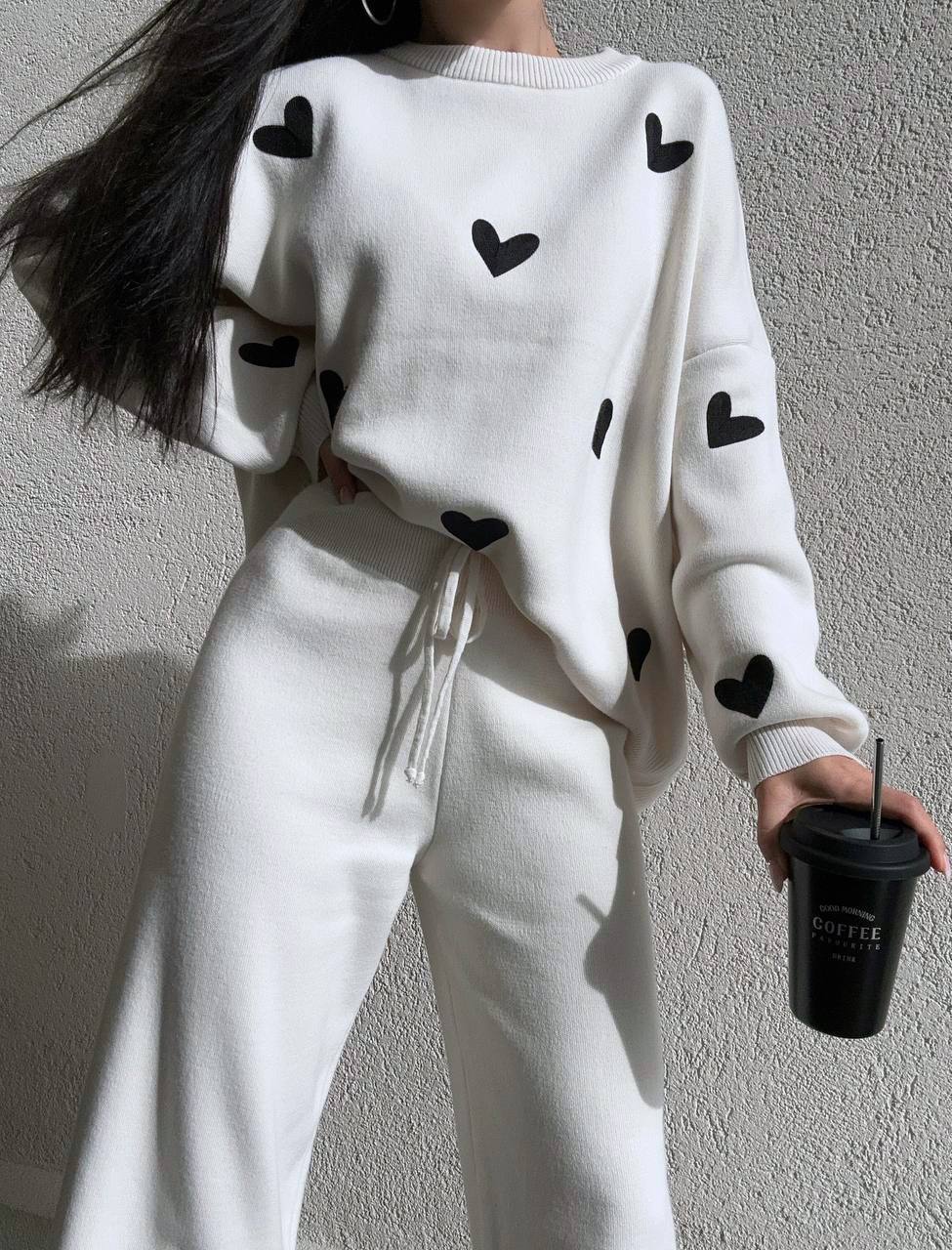 Person wearing a white sweater with black heart patterns against a plain background