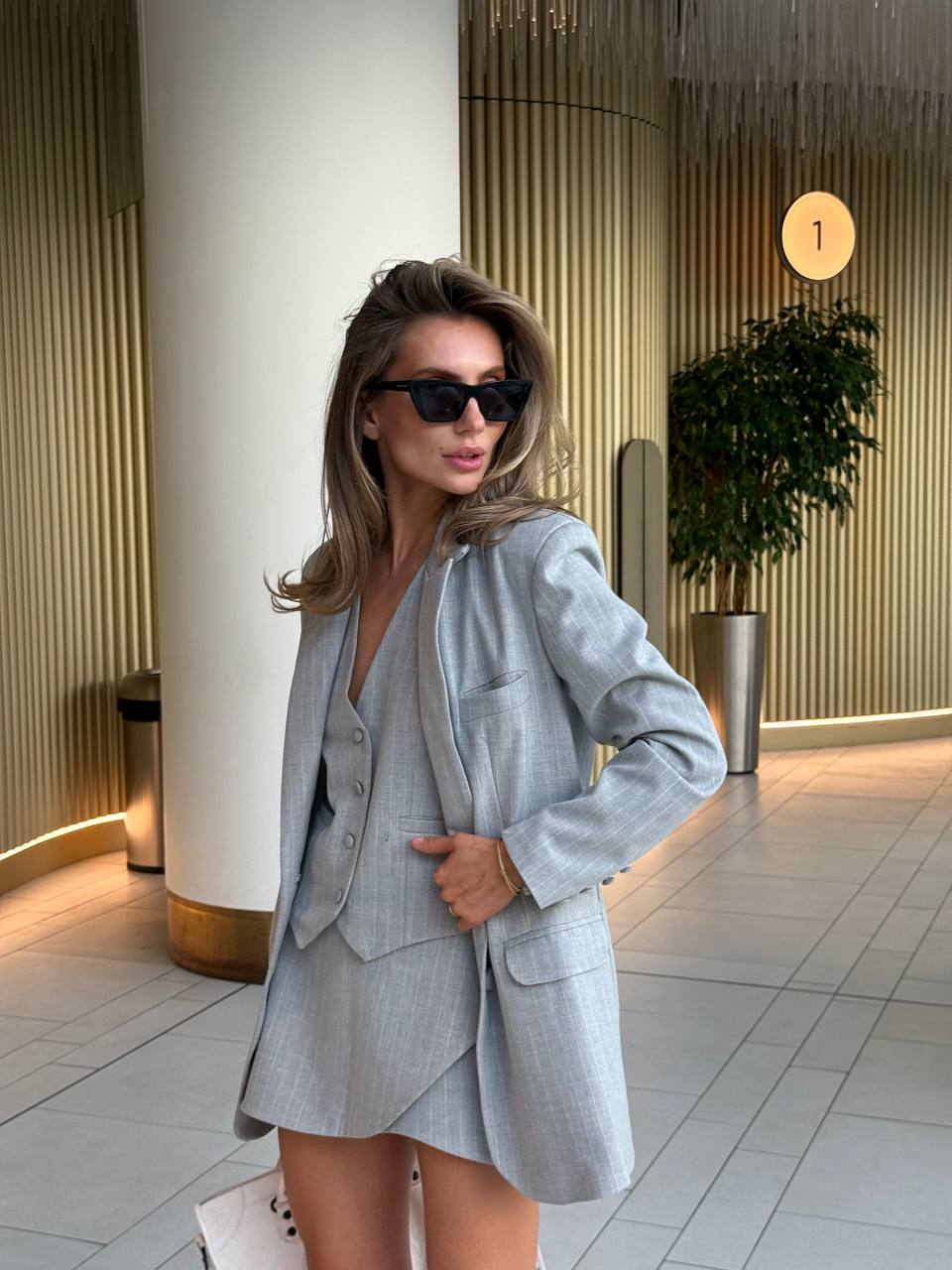 Woman in a gray suit standing in an indoor setting with modern decor.