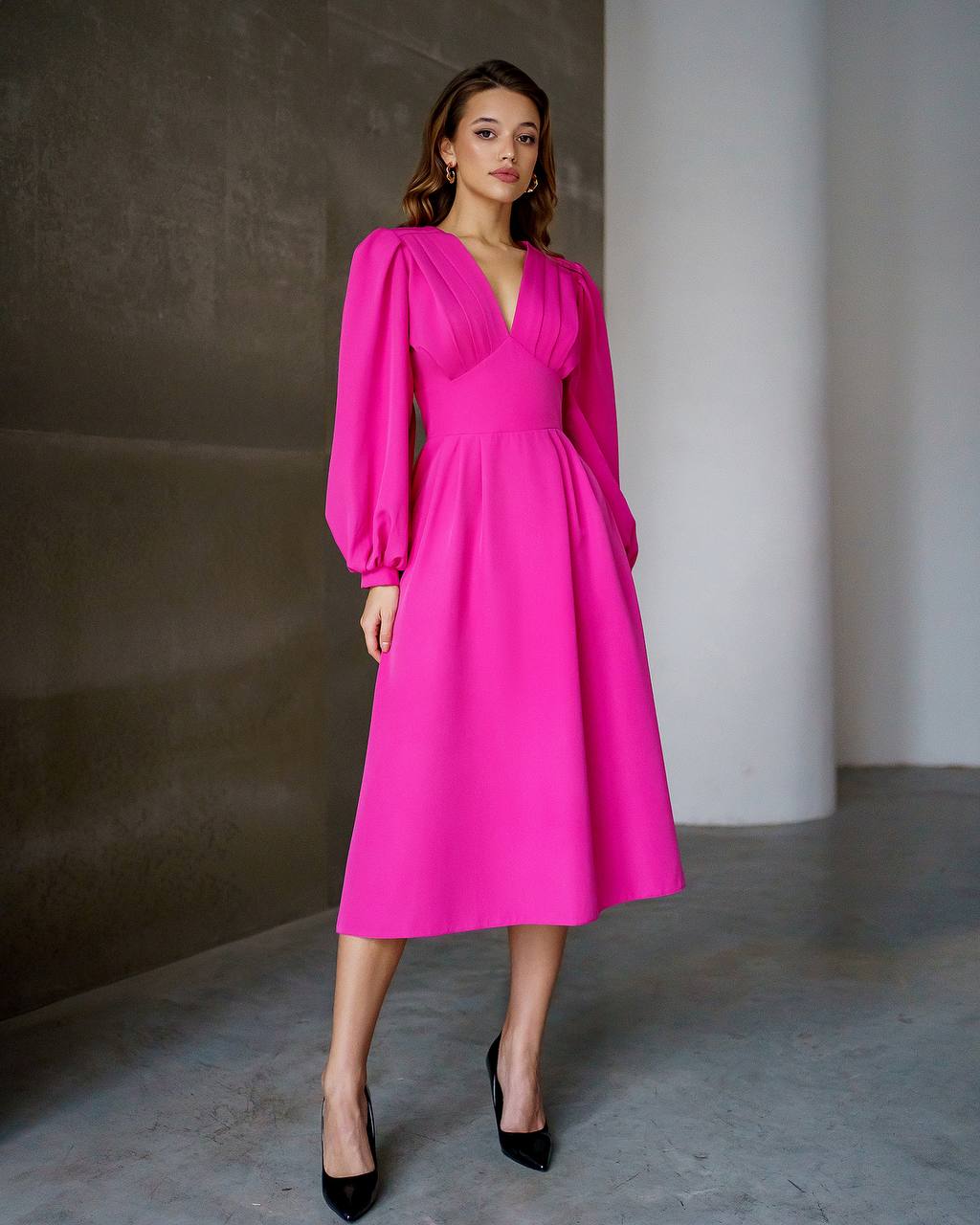 Woman wearing a bright pink dress with long sleeves in a minimalistic setting.