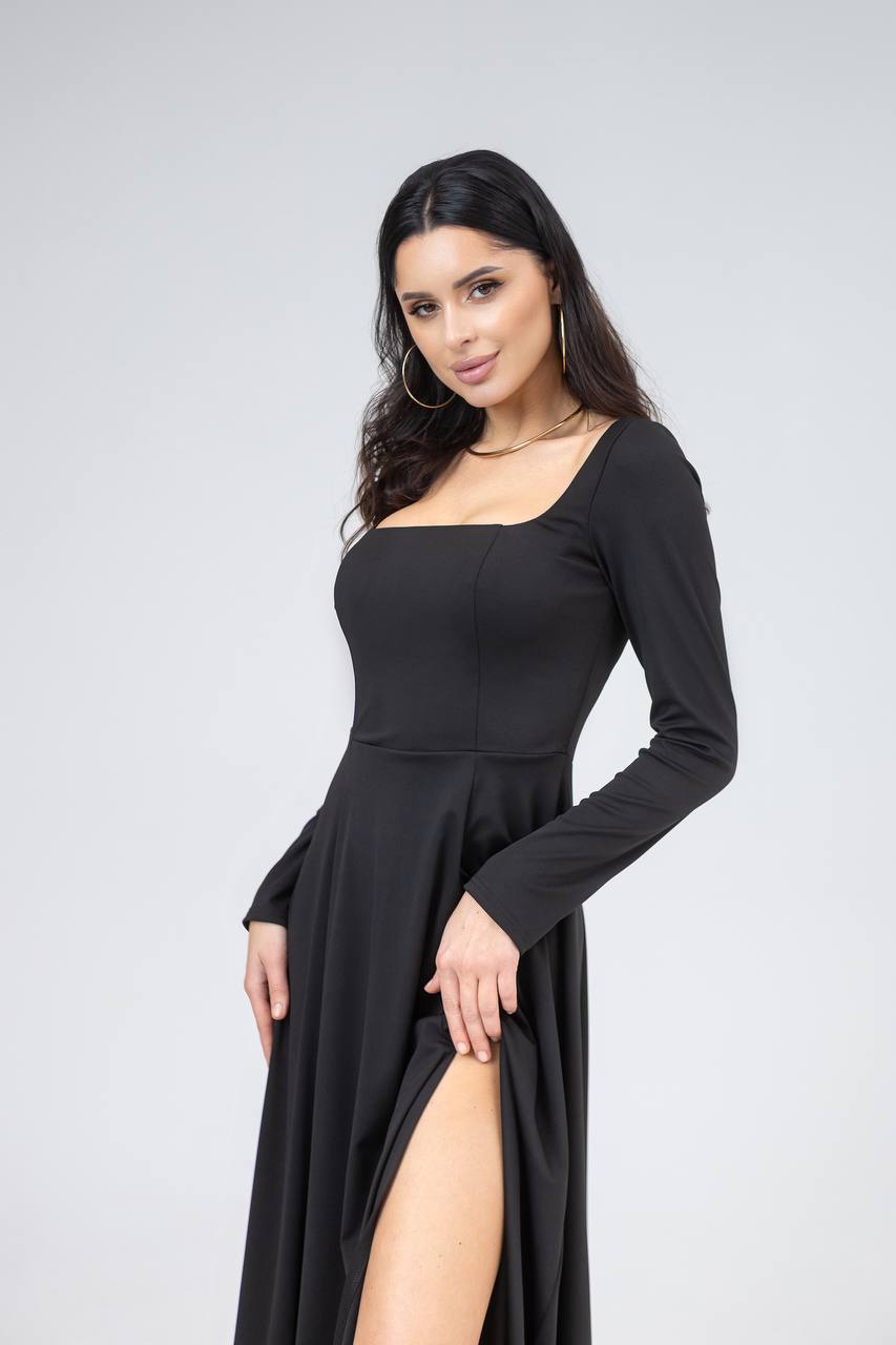 Woman wearing a black long-sleeve dress with a slit on a light gray background