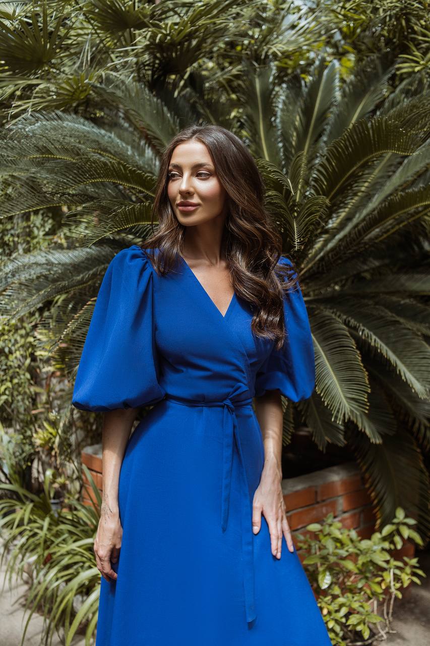 Woman in a blue dress standing in front of green foliage