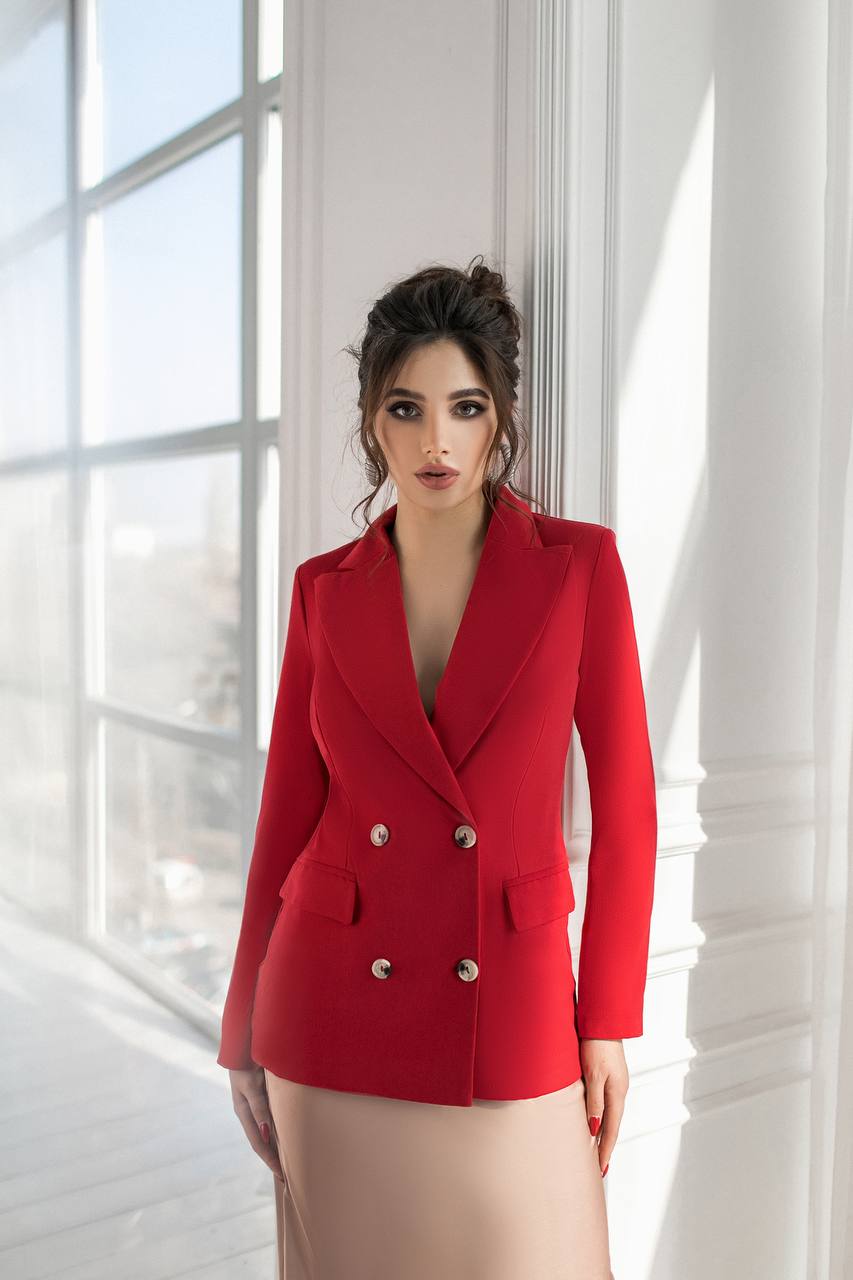 Woman wearing a red blazer in a bright room with large windows.