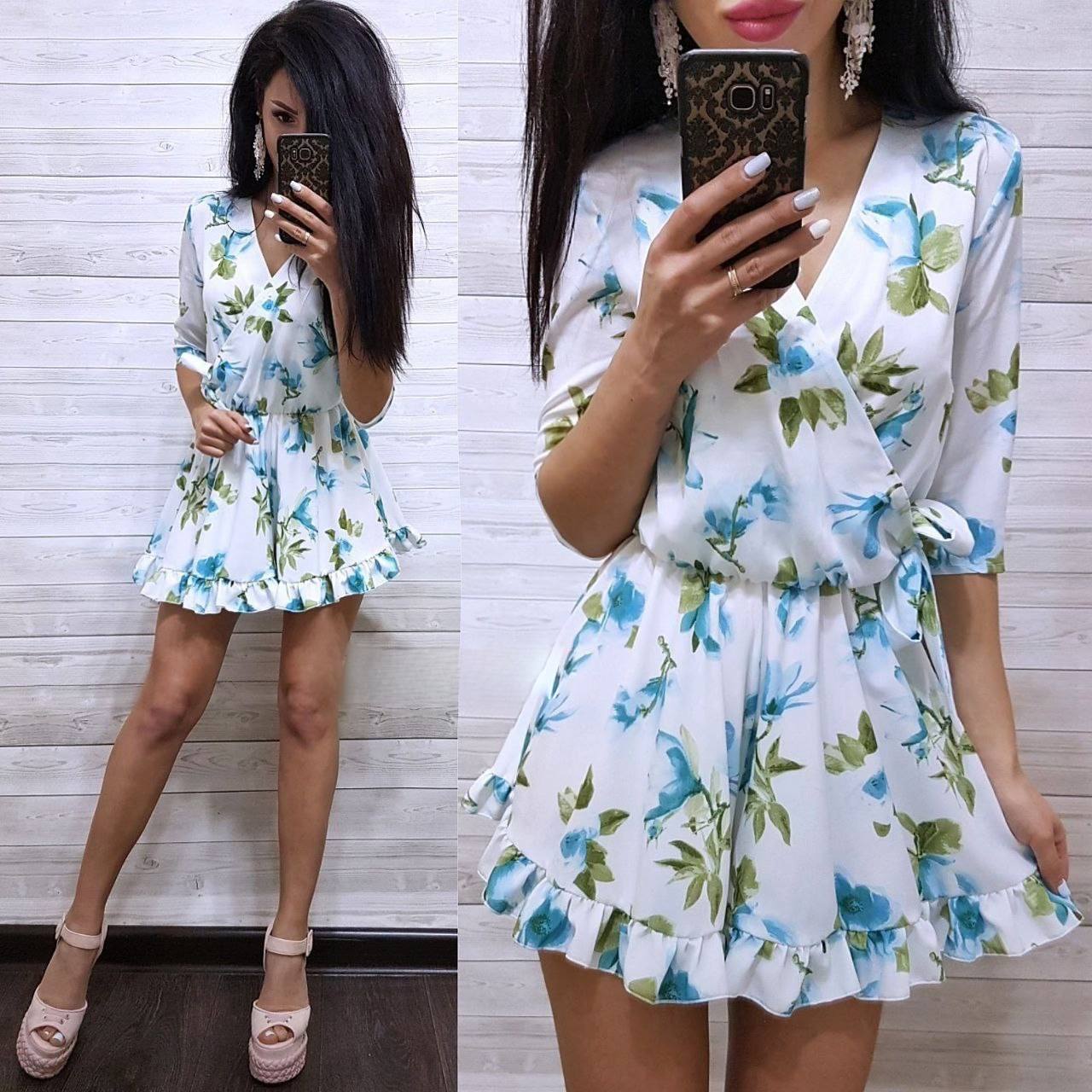 Woman wearing a floral dress taking a mirror selfie against a wooden panel background