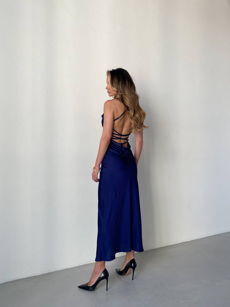 Woman wearing a blue dress with cut-out back against a white wall
