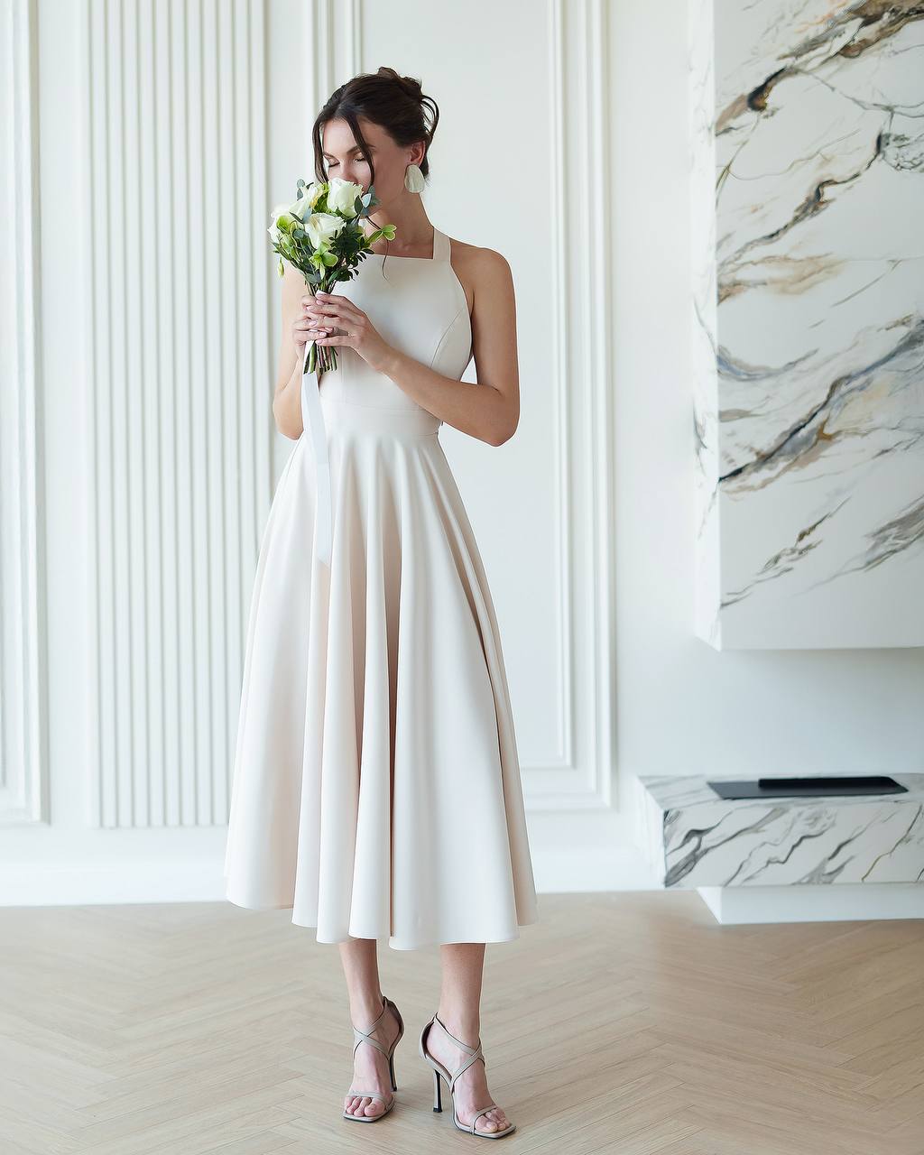 Woman in a white dress holding flowers in a room with marble wall.