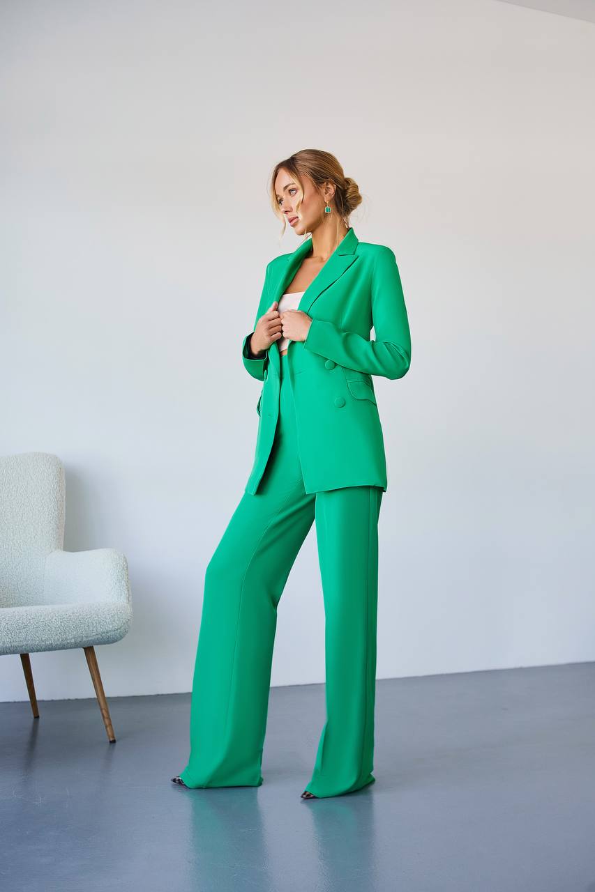Woman wearing a green suit standing in a minimalistic room with a gray chair.