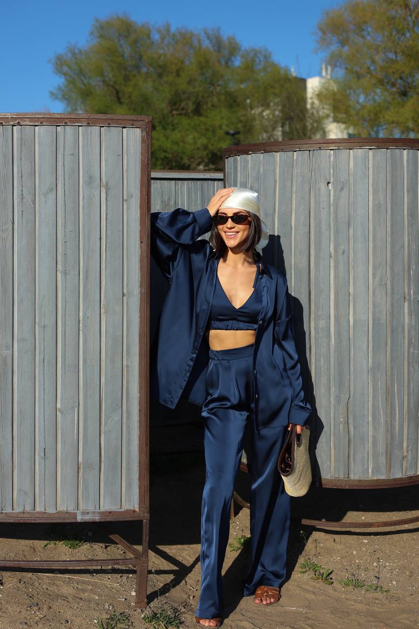 Woman in a blue outfit standing next to metal tanks with trees in the background