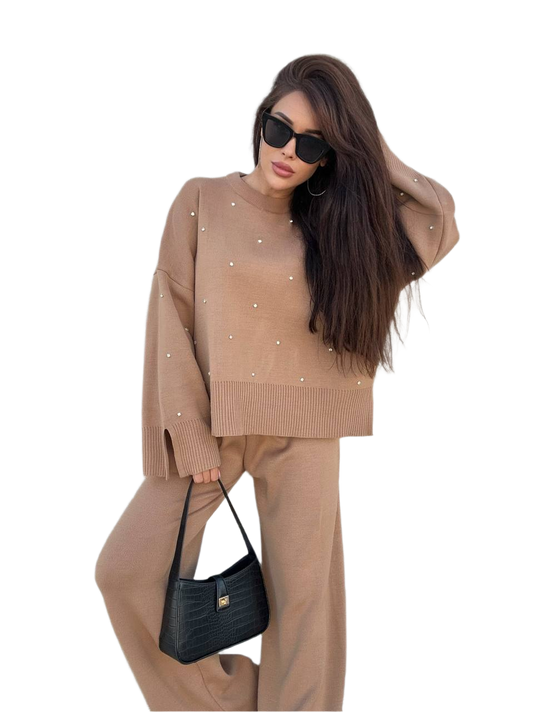 Woman wearing a beige sweater and pants with a black handbag on a white background