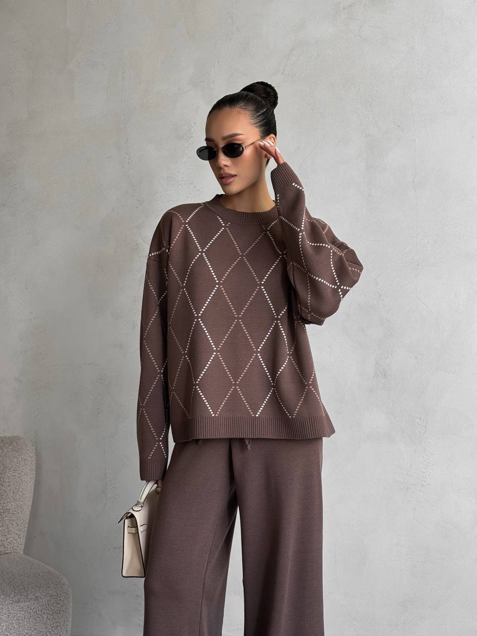Woman wearing a brown argyle sweater and pants against a gray background