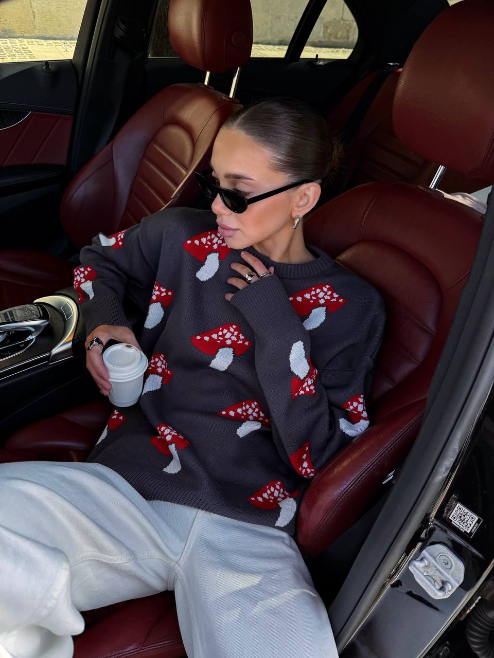 Person sitting in a car wearing a sweater with red and white patterns