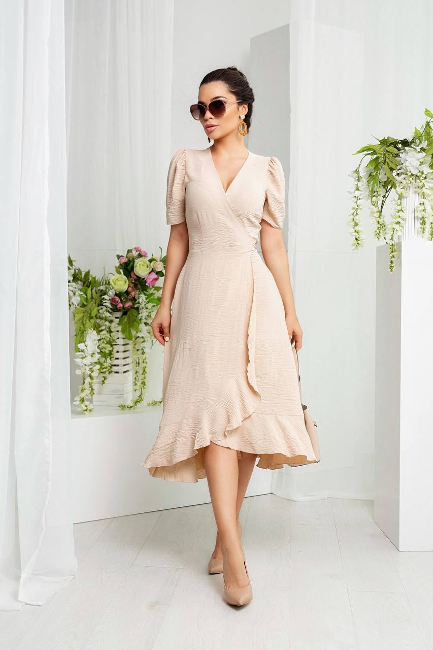 Woman wearing a beige dress standing in a bright room with plants.