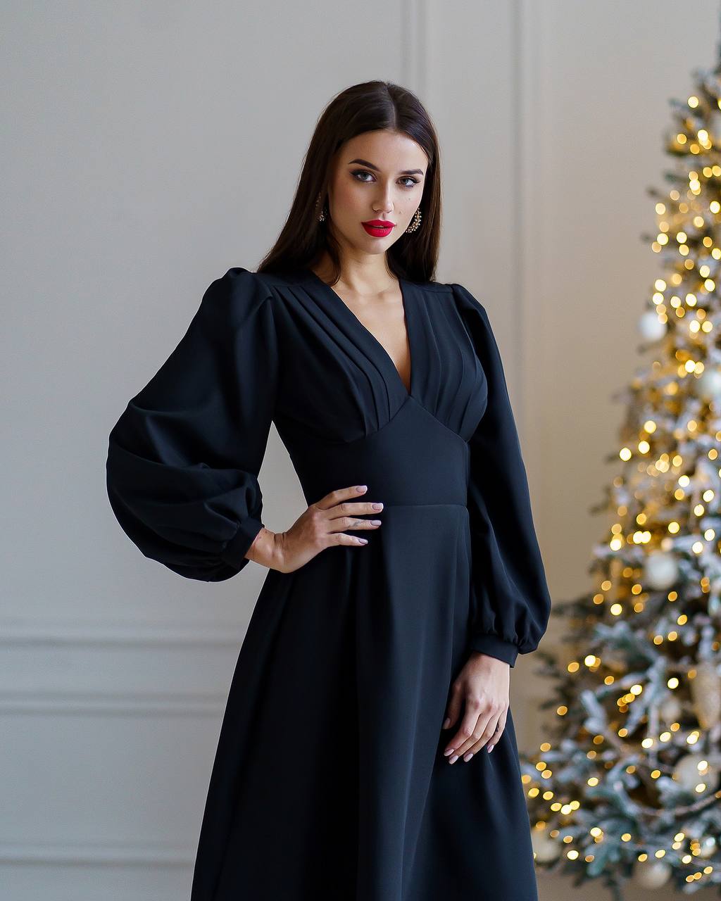 Woman in a black dress standing in front of a decorated Christmas tree.