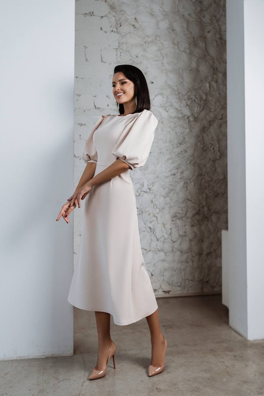 Woman in a white dress standing against a textured wall.