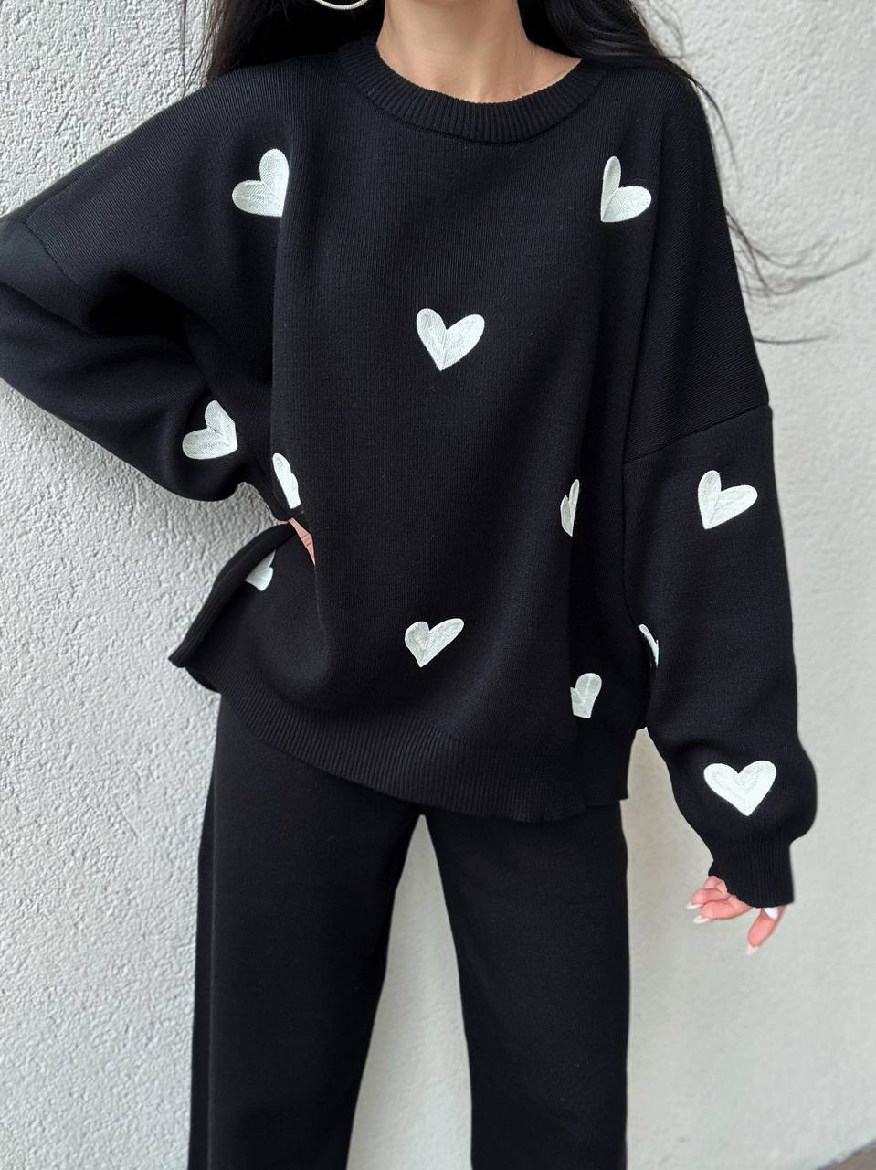 Black sweater with white heart patterns worn by a person against a light gray background