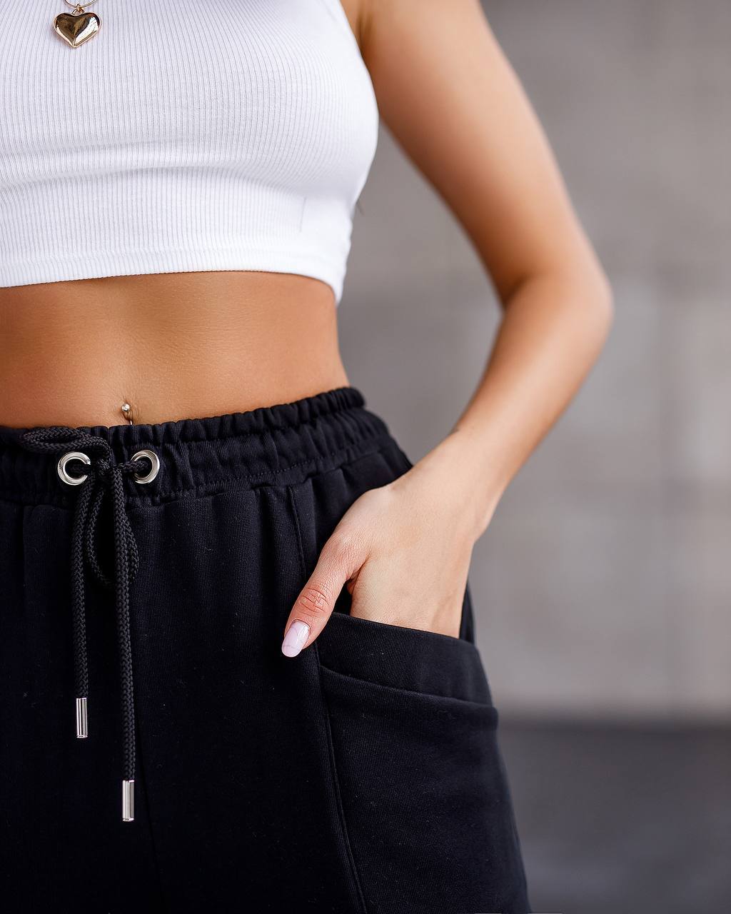 Person wearing black pants with drawstring and white cropped top against a blurred background