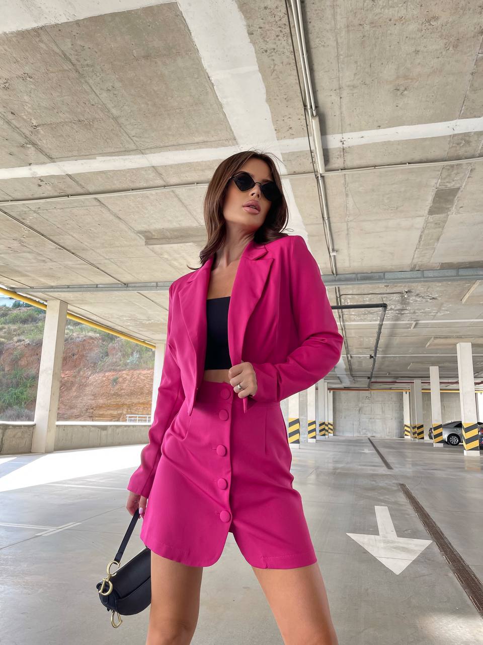 Woman in a bright pink outfit standing in an underground parking garage.