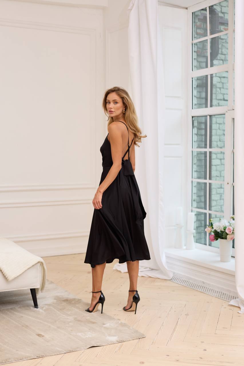 Woman in a black dress standing in a bright room with large windows.
