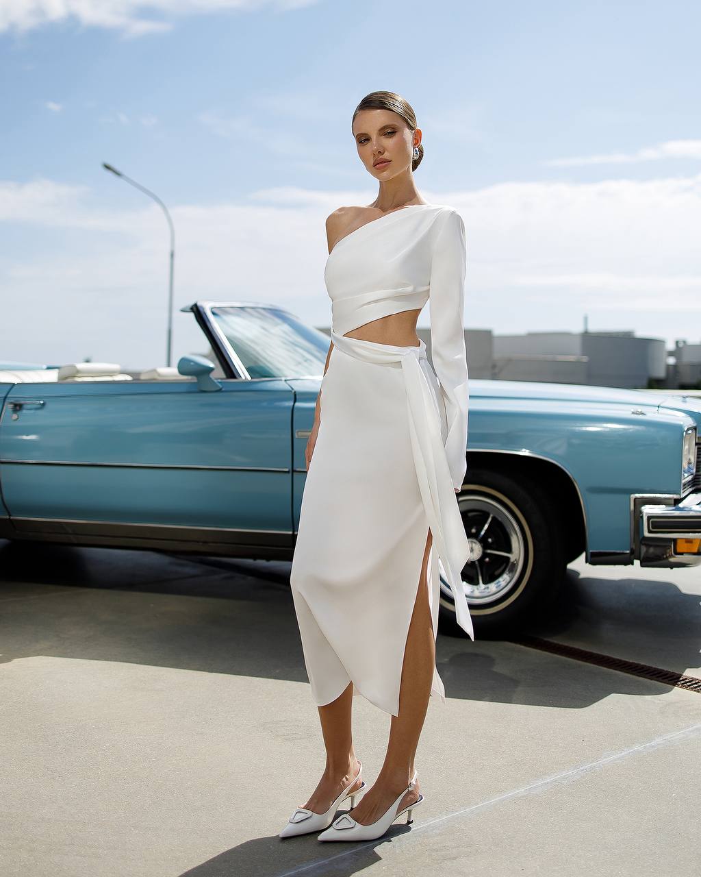 Woman in a white dress standing in front of a blue vintage car.