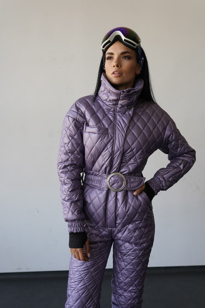 Person wearing a purple quilted snowsuit with goggles on a plain background