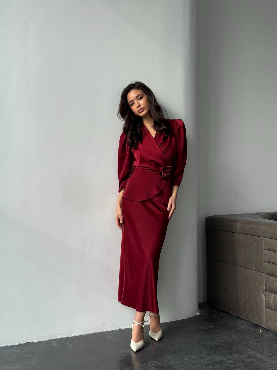 Woman in a burgundy outfit standing against a gray wall.