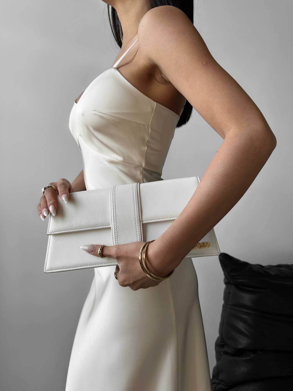 Woman in a white dress holding a white clutch against a neutral background