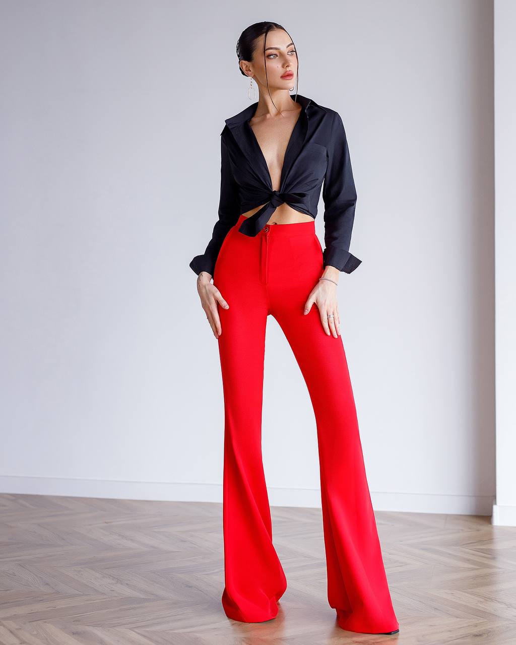 Woman wearing a black top and red pants against a white background