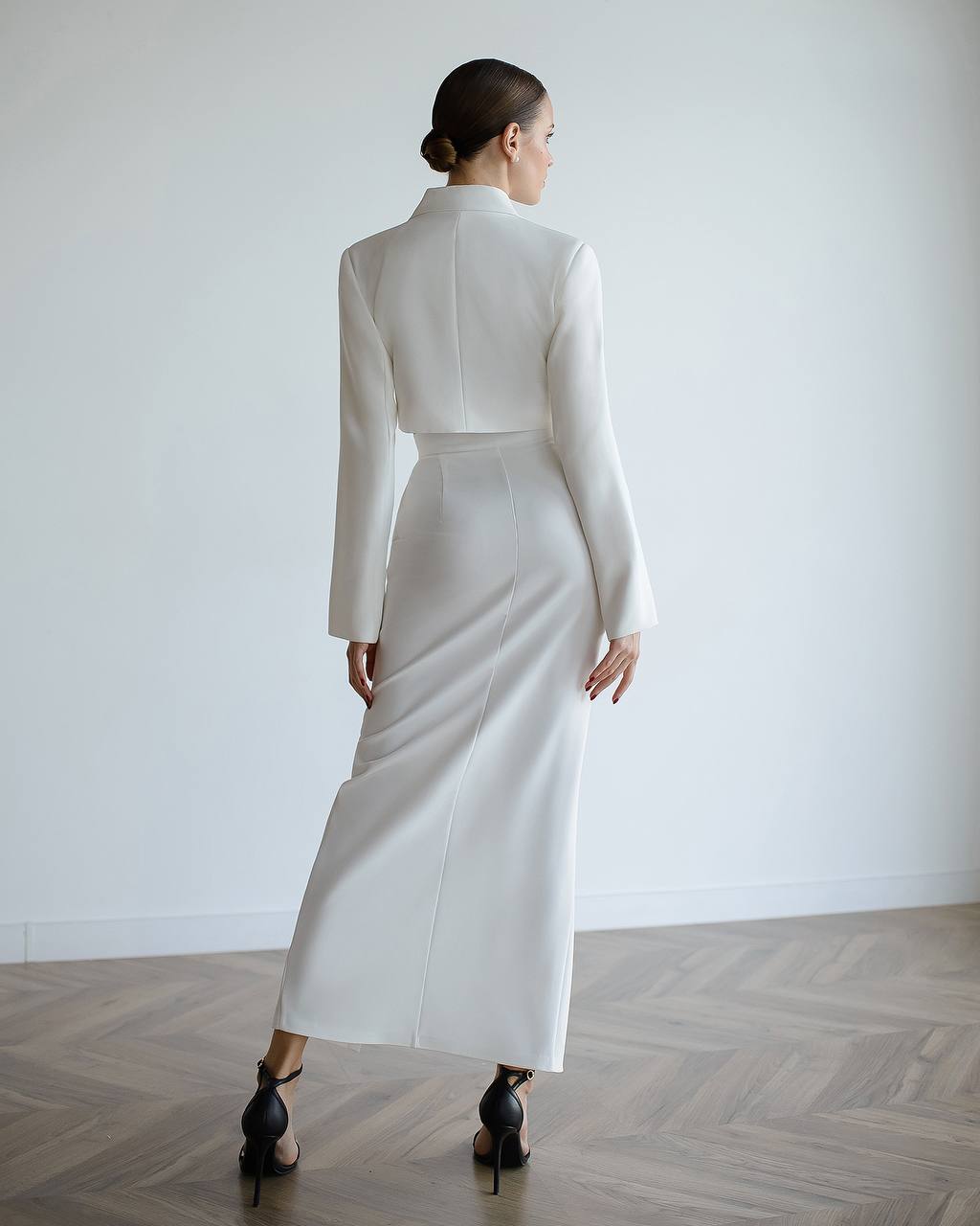 Woman wearing a white outfit standing against a plain white wall.