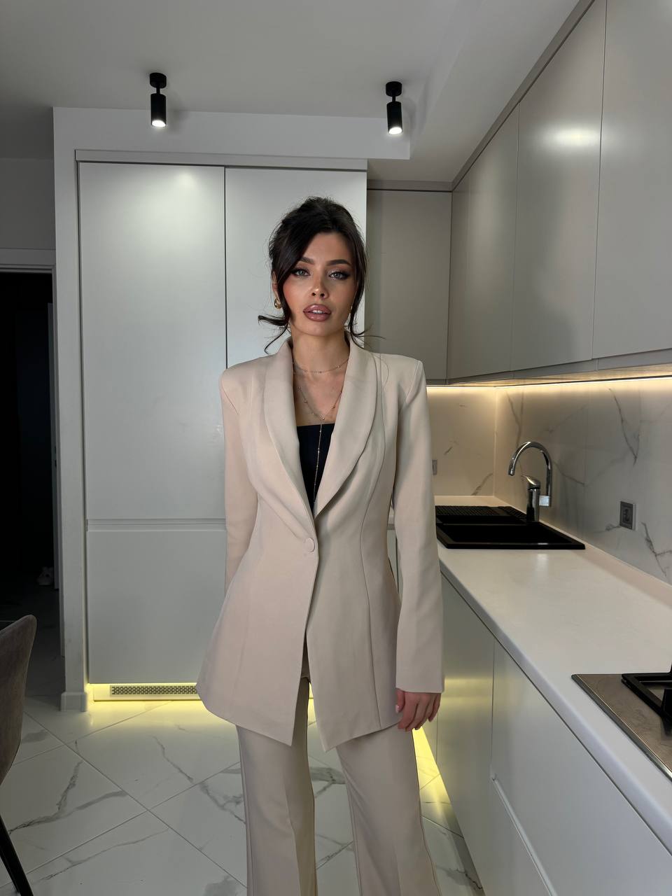 Woman in a beige suit standing in a modern kitchen.