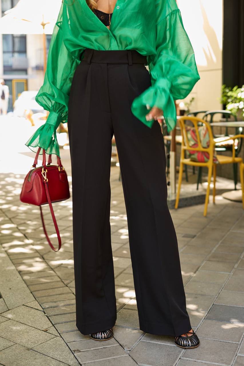 Person wearing a green blouse and black pants outdoors on a sunny day.