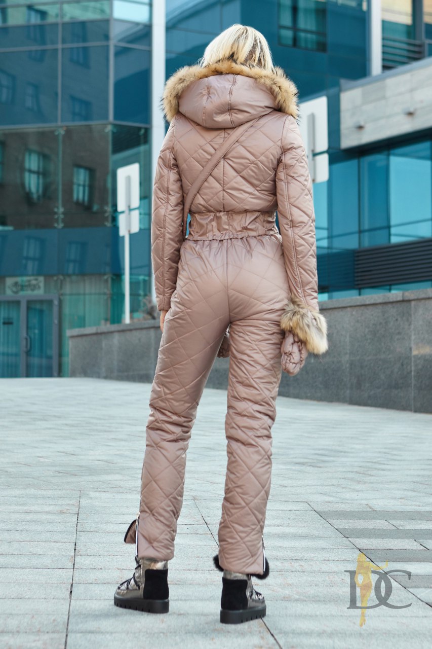 Person wearing a beige quilted jumpsuit with fur trim in an urban setting