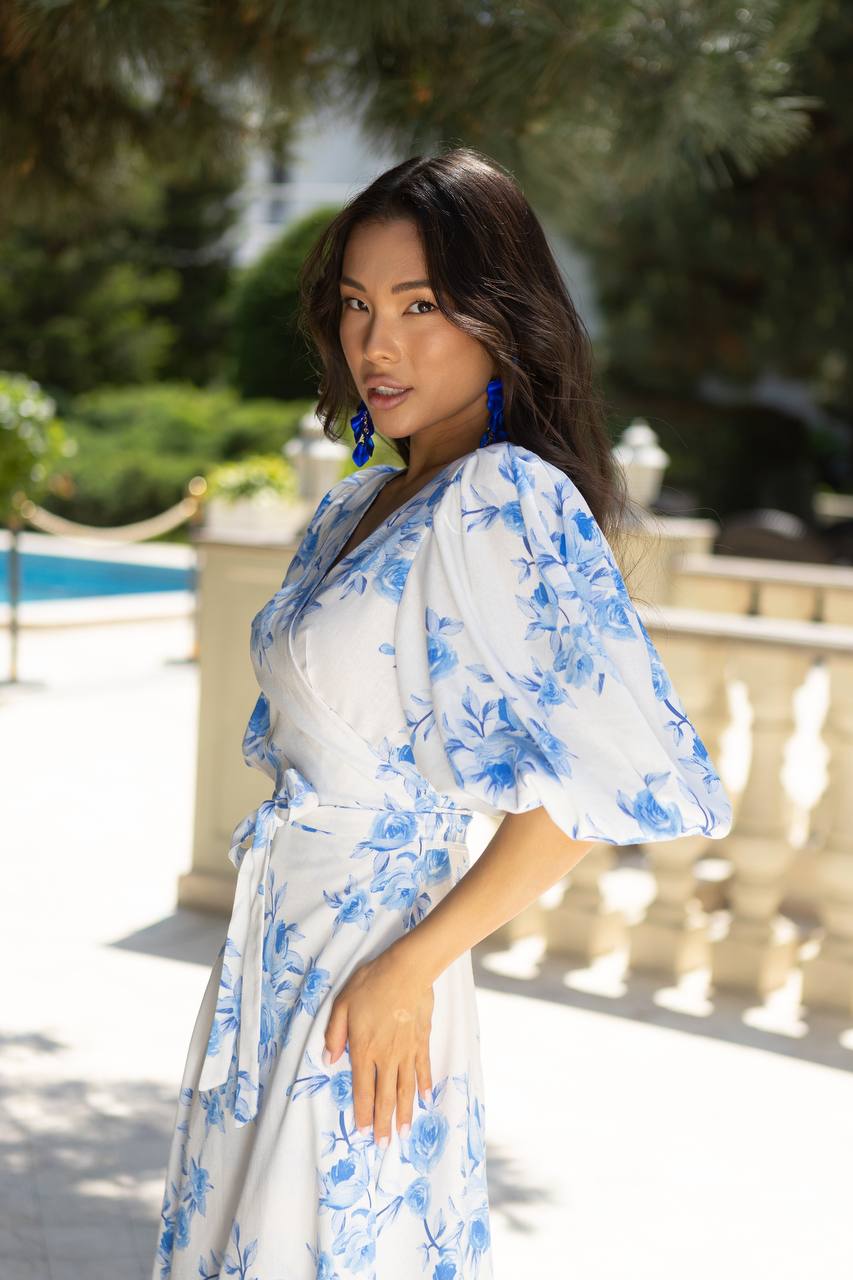 Woman wearing a blue floral dress standing outdoors with greenery in the background