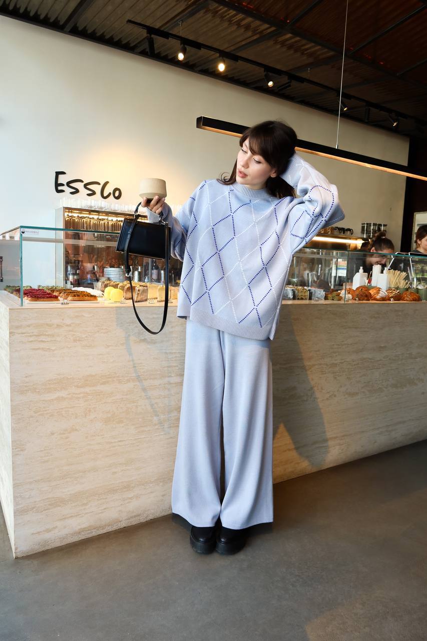 Woman in a light blue sweater and pants standing in a cafe with 'Essco' branding.