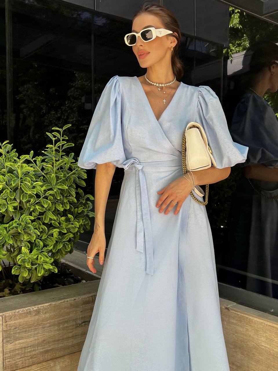 Woman in a light blue dress with puffed sleeves standing outdoors.