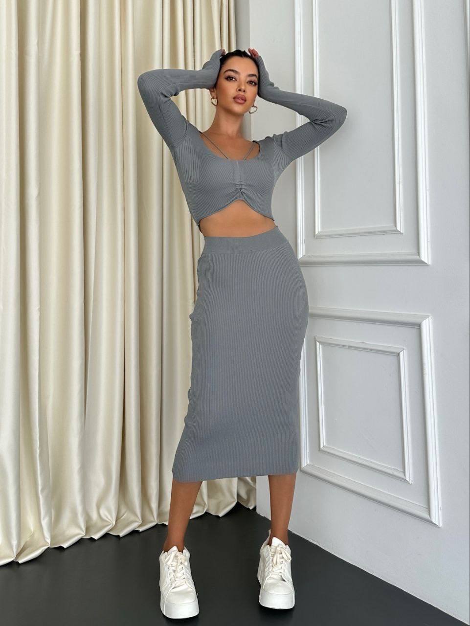 Woman wearing a gray outfit with a matching skirt and top in a room with white walls and curtains.