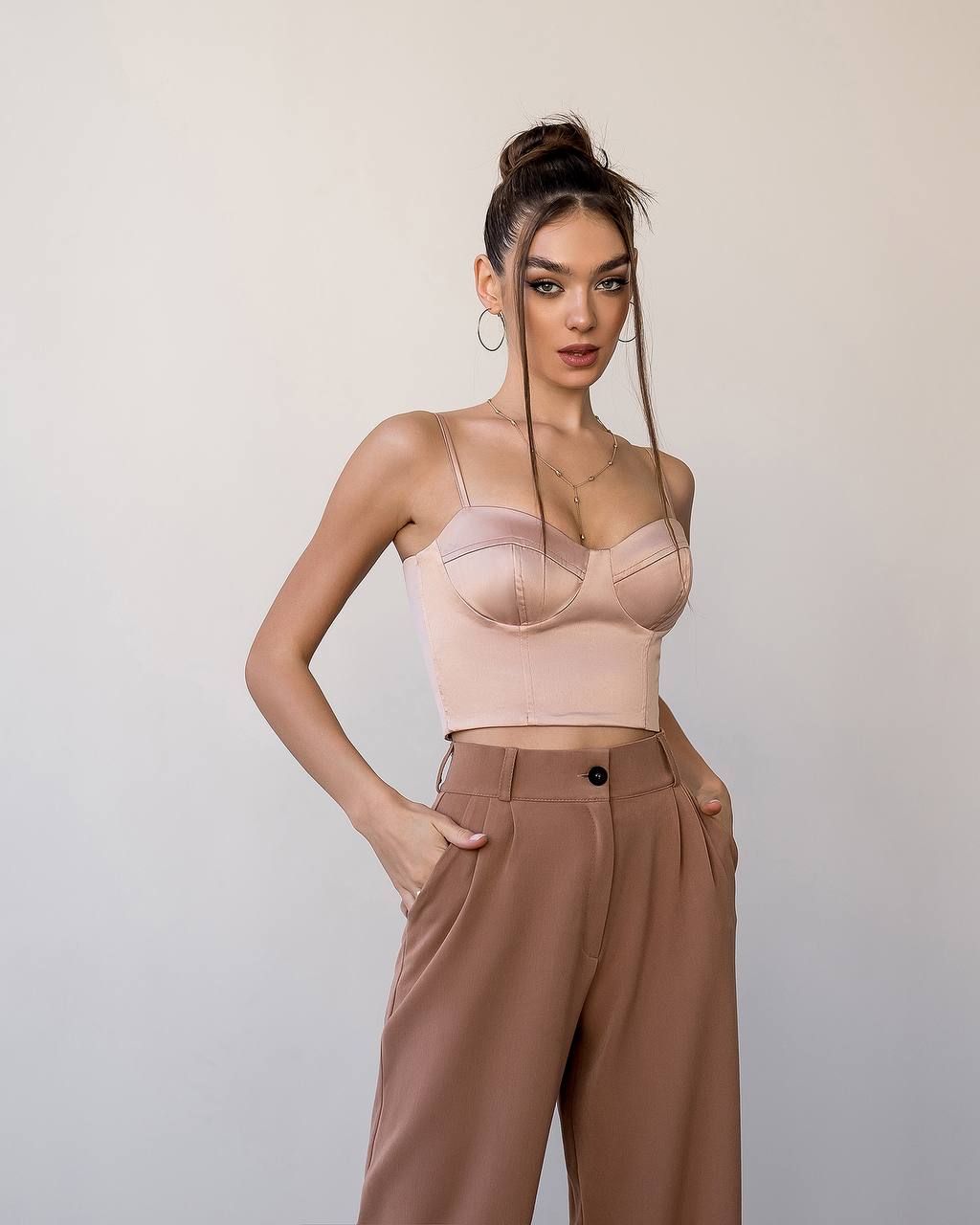 Woman wearing a beige top and brown pants against a plain background