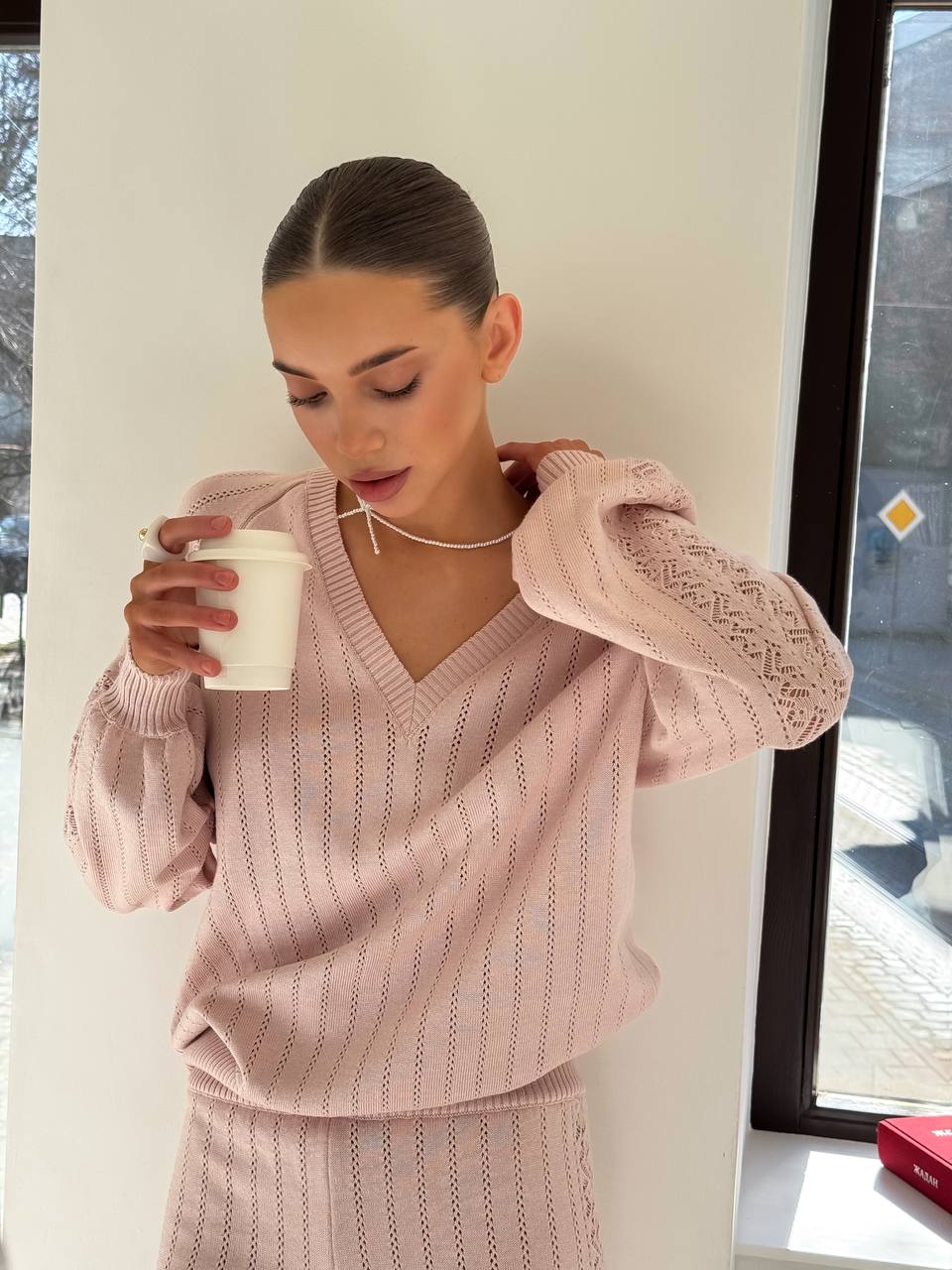 Woman in a pink knit outfit holding a white mug indoors.