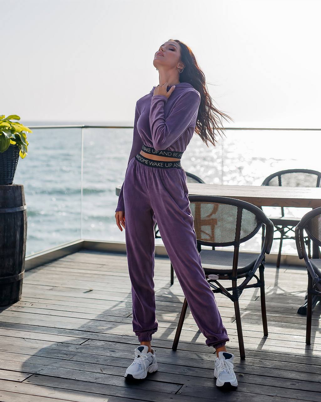 Woman in a purple tracksuit standing on a wooden deck by the water.