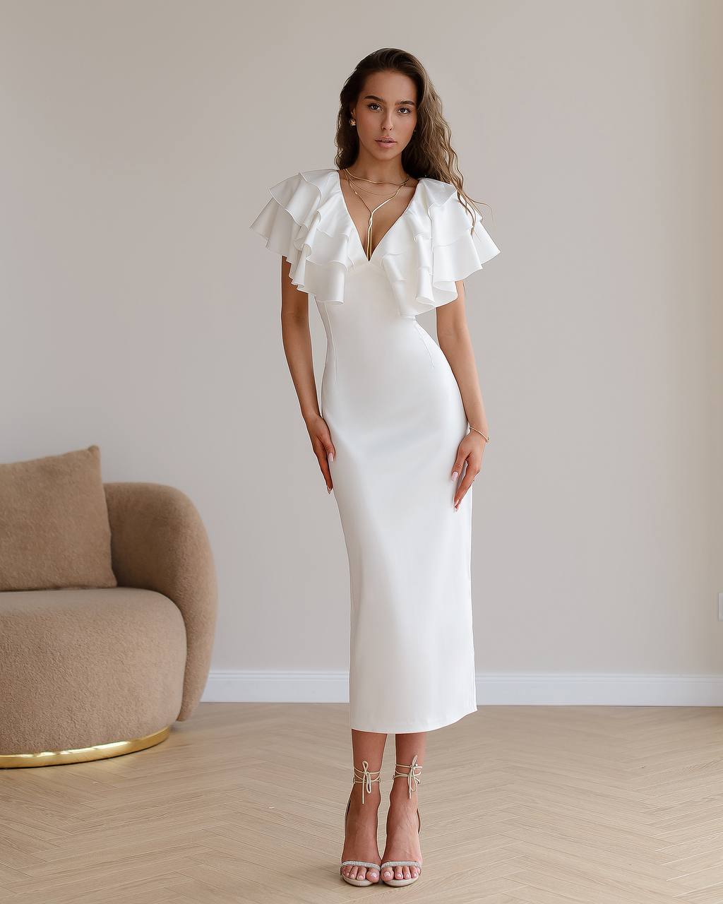 Woman wearing a white dress with ruffled sleeves in a minimalistic room.