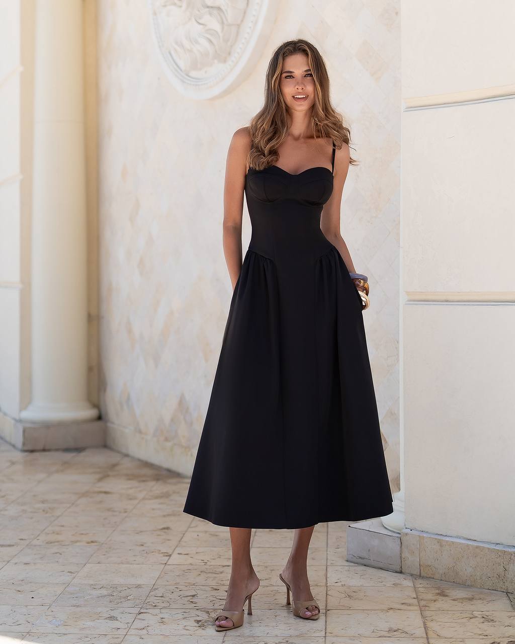 Woman wearing a black dress standing in an elegant indoor setting.