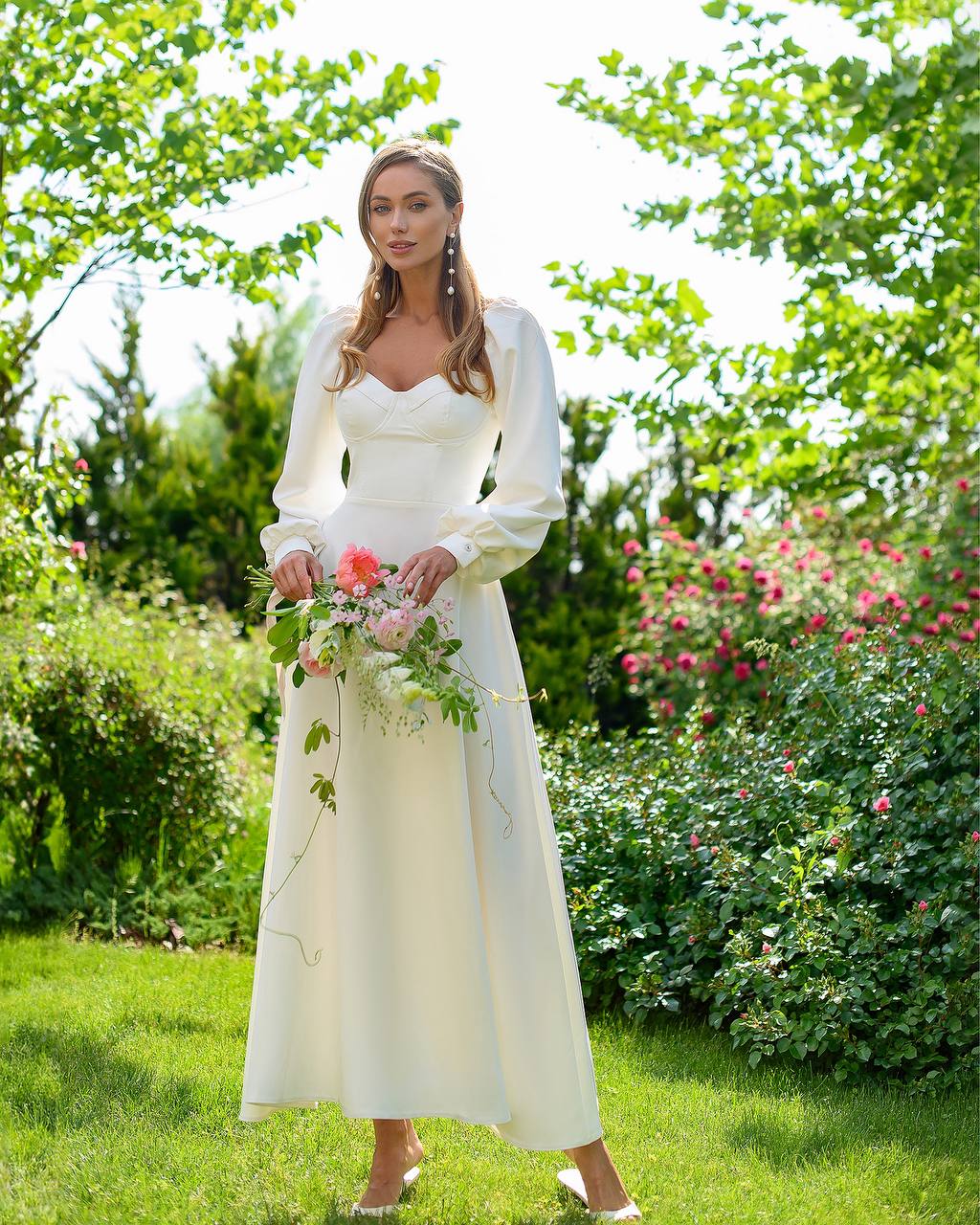 Woman in a white dress holding flowers in a garden setting