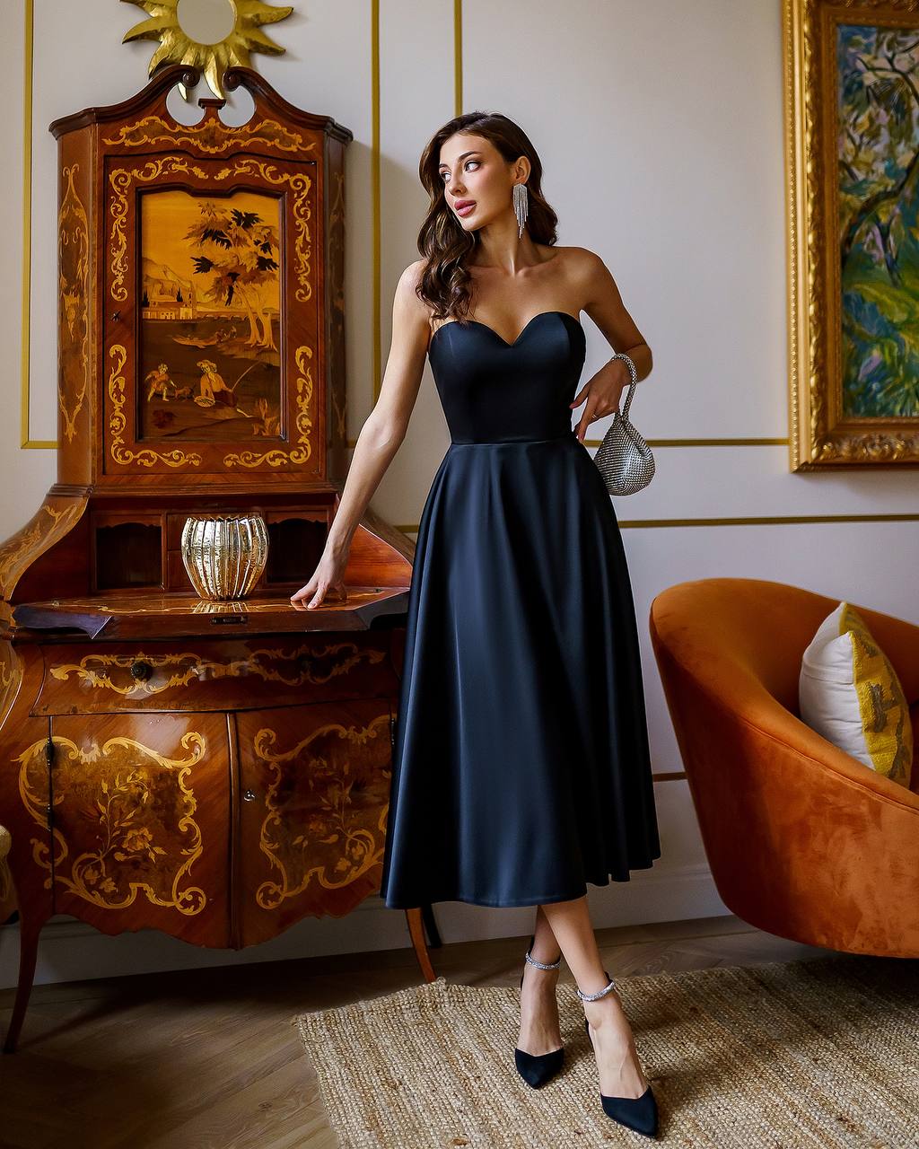 Woman in a black dress standing in an elegant room with decorative furniture and art.