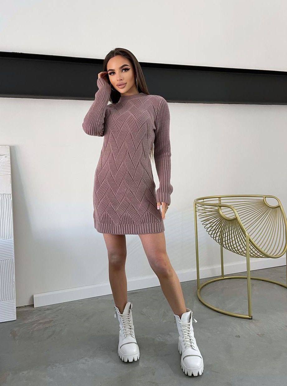 Woman wearing a mauve sweater dress with white sneakers in a minimalistic room.