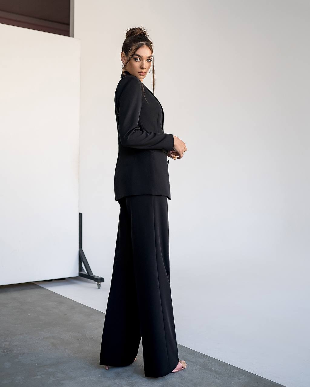 Woman wearing a black outfit standing against a white wall.