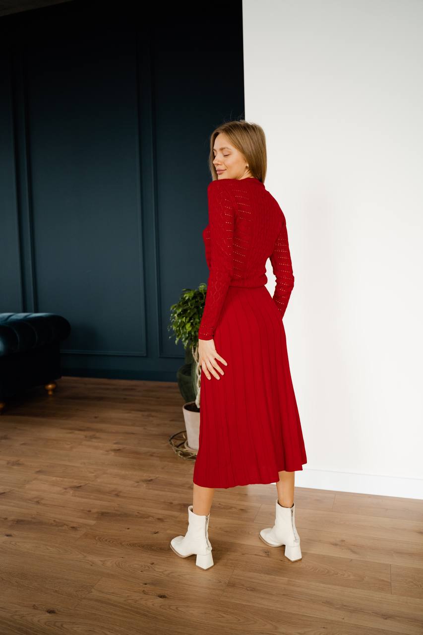 Woman in a red dress standing in a room with wooden floor and white wall.