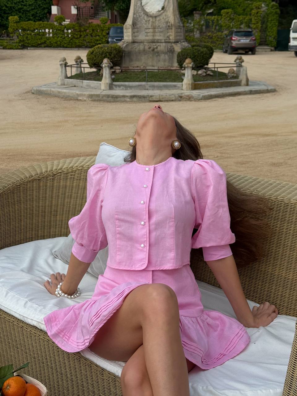 Woman in a pink outfit sitting on a wicker chair with a scenic background