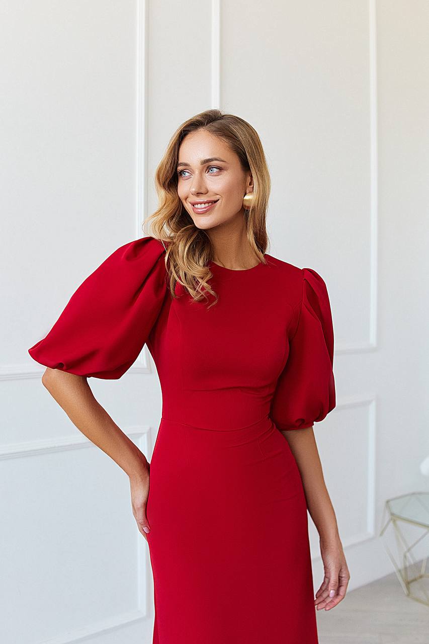 Woman wearing a red dress with puff sleeves against a white wall