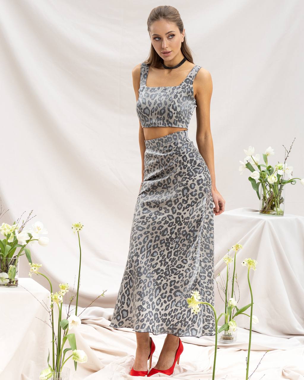 Woman wearing a leopard print two-piece outfit with red shoes in a minimalistic setting.