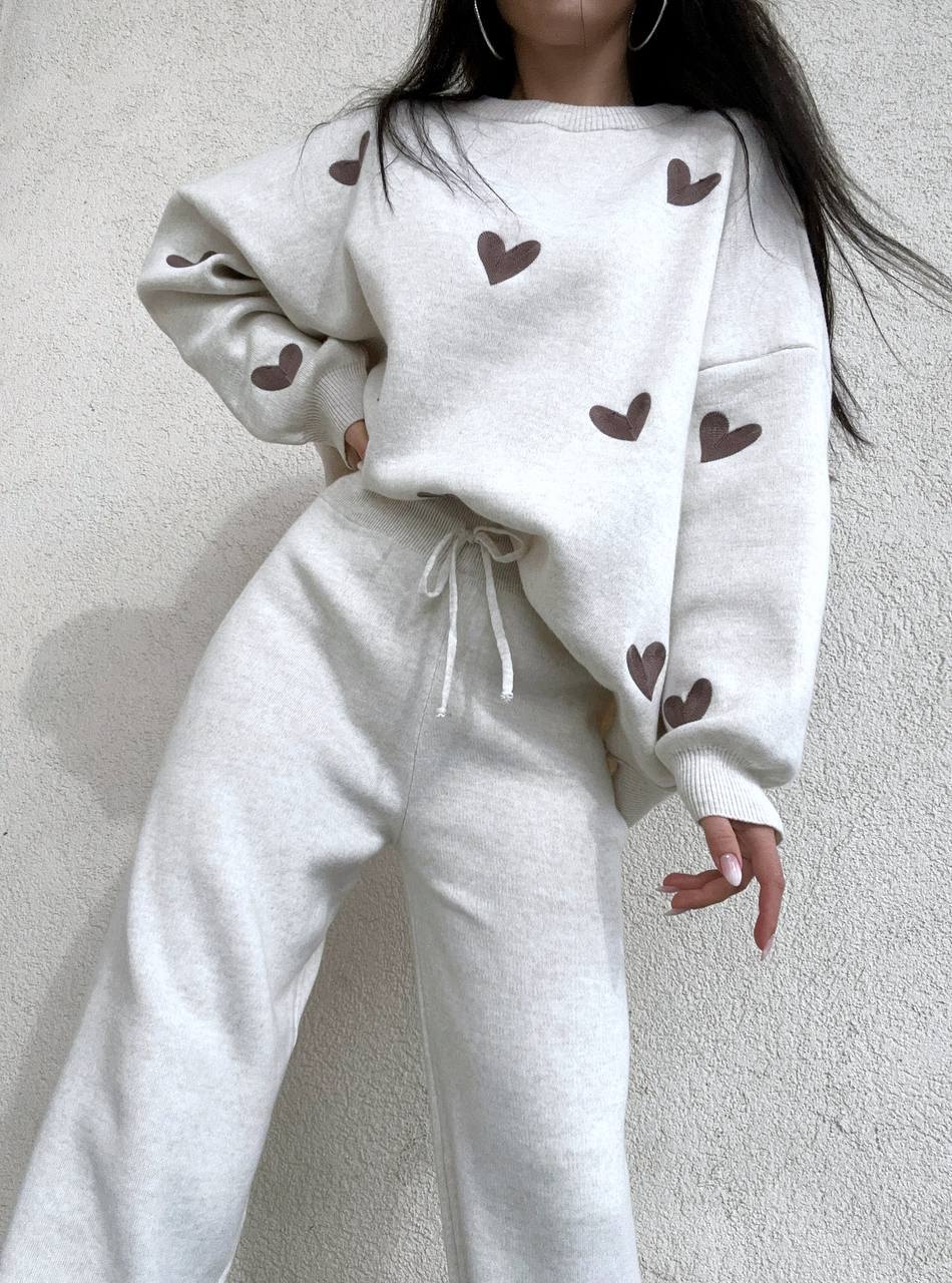 White sweatshirt and pants set with brown heart patterns on a neutral background