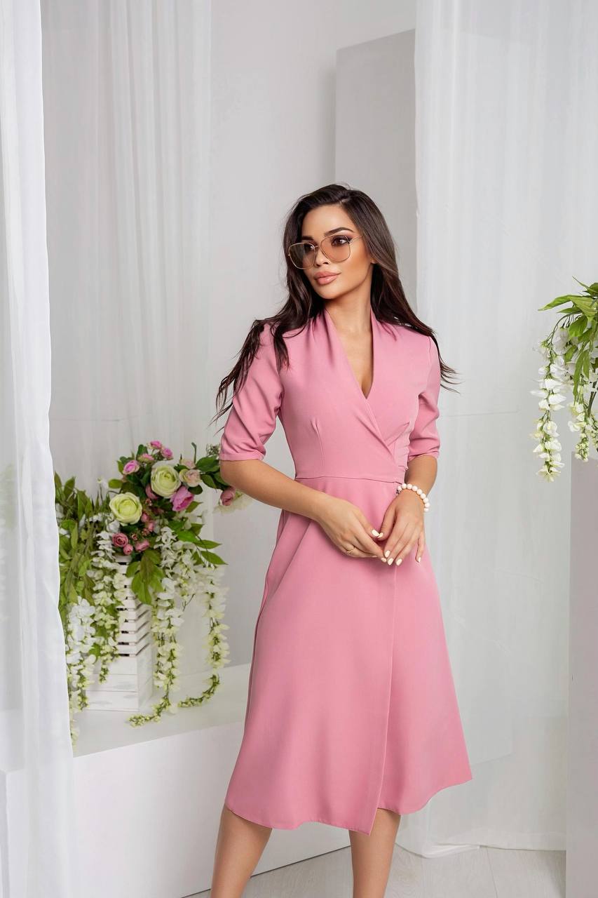 Woman wearing a pink dress standing in a room with white curtains and floral decorations.
