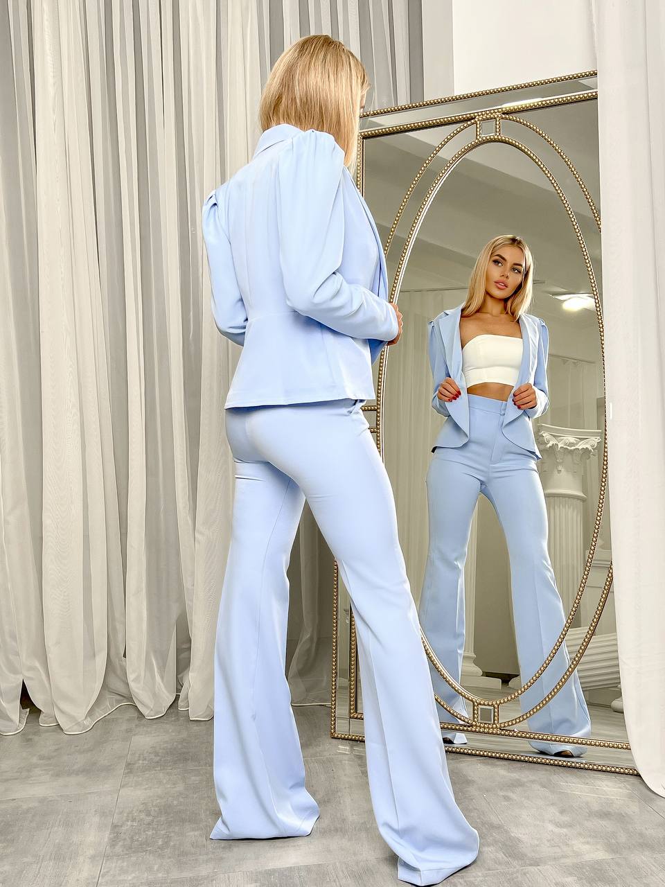 Woman in light blue outfit standing in front of a mirror.